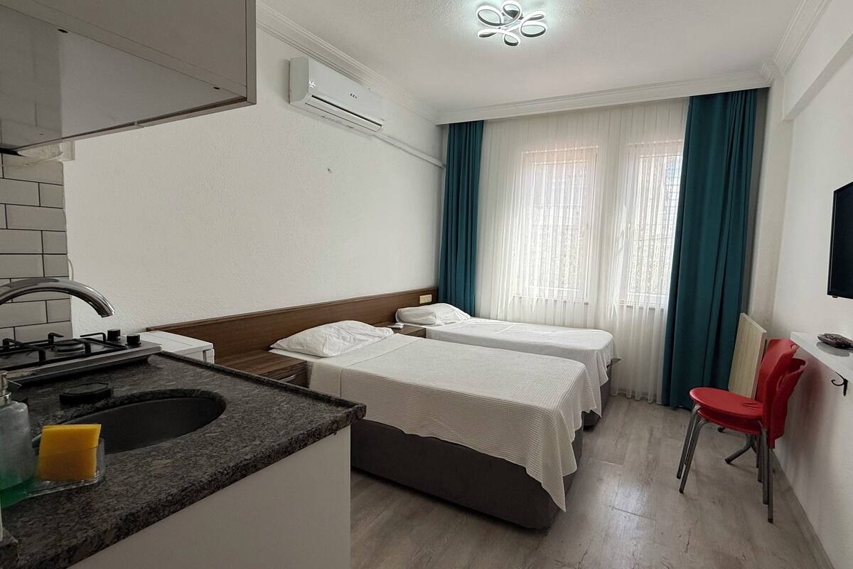 A hotel room with a kitchenette, two beds, a TV, and a window with curtains.