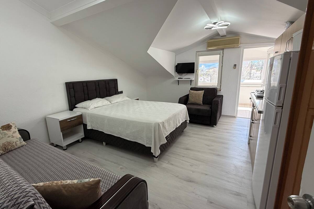 A bedroom with a bed, bedside table, chair, and a view of the outside.