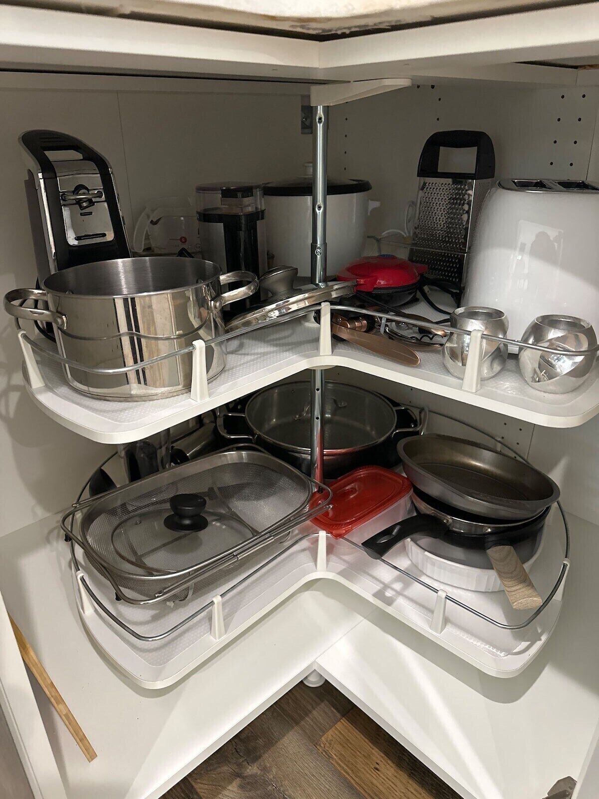Una cocina con un mueble de esquina que contiene ollas, sartenes y un rallador.