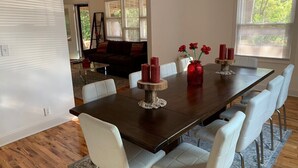 Comedor con una mesa de madera oscura, sillas blancas y un jarrón con flores rojas.