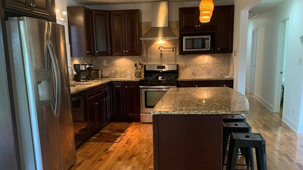 Una cocina moderna con armarios de madera oscura, electrodomésticos de acero inoxidable, encimera de granito y suelo de madera en espiga.