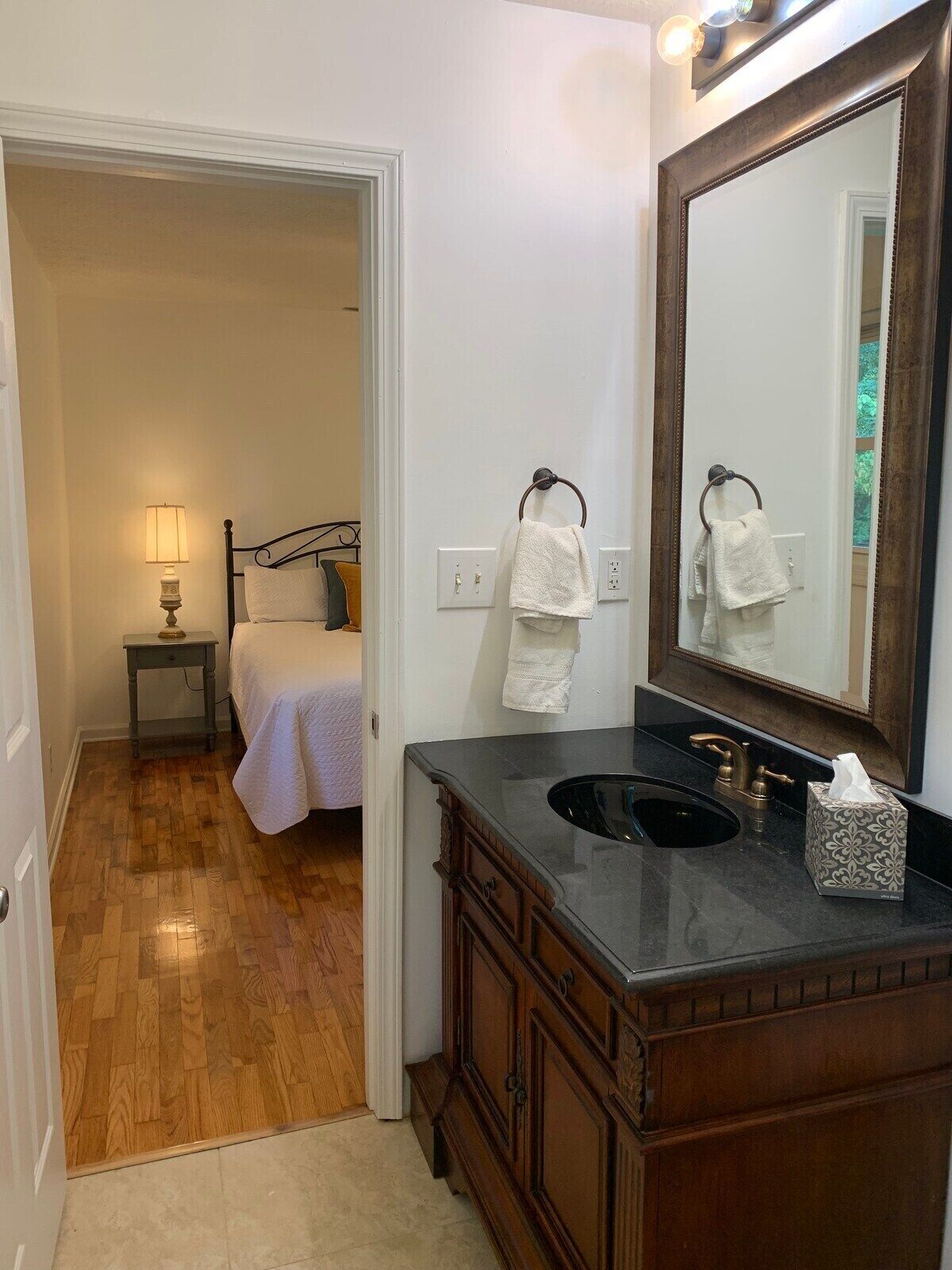 A bathroom with a wooden vanity, a large mirror, and a sink. There is a towel rack with two towels and a tissue box on the vanity.