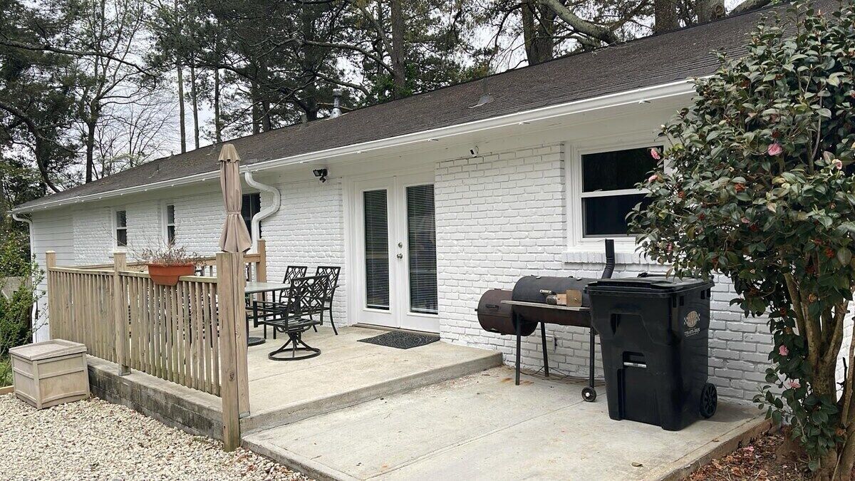 A white house with a porch, a grill, and a patio with outdoor furniture.