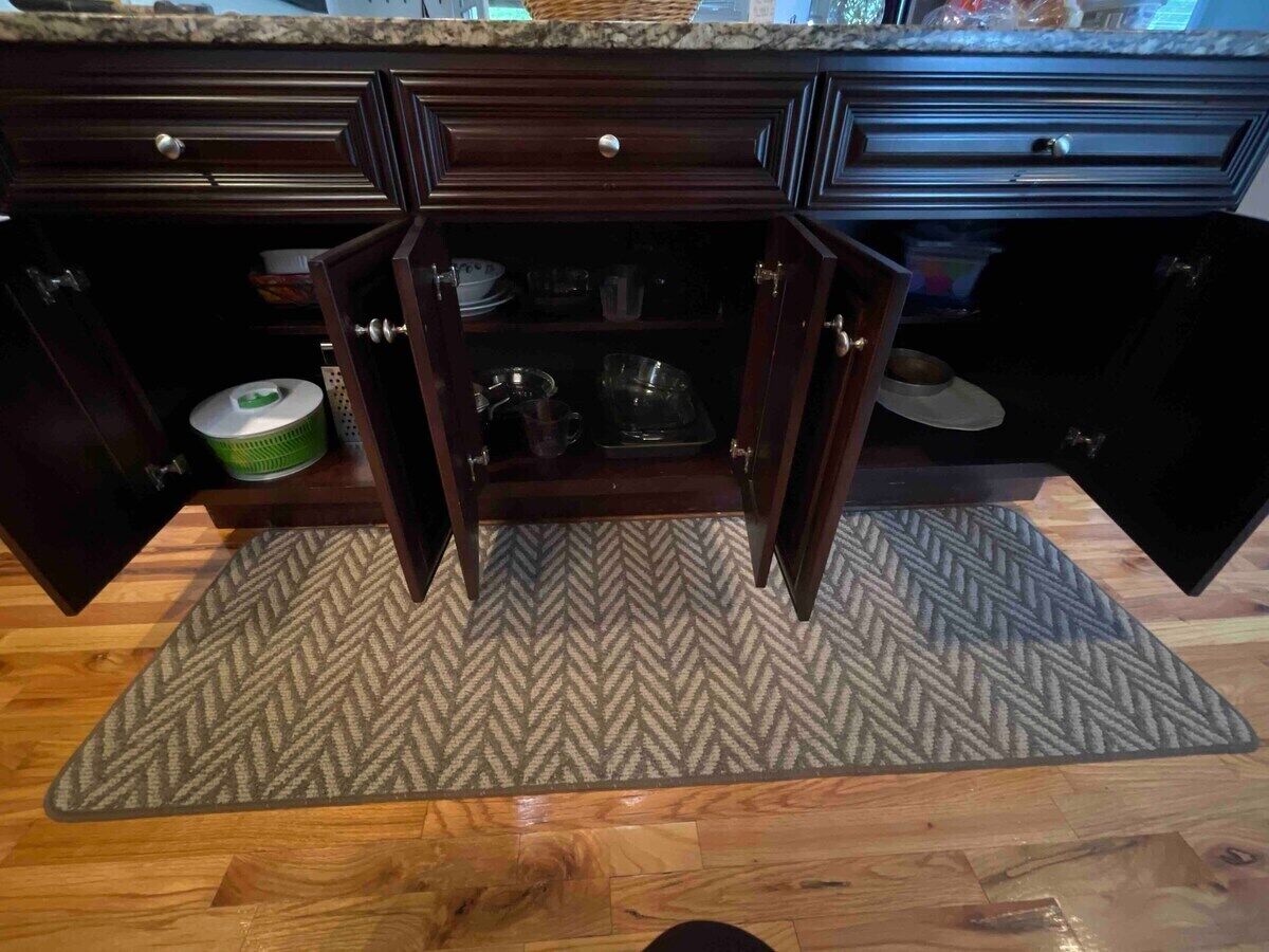 Una cocina con armarios de madera, alfombra con estampado de espiga y piso de madera.