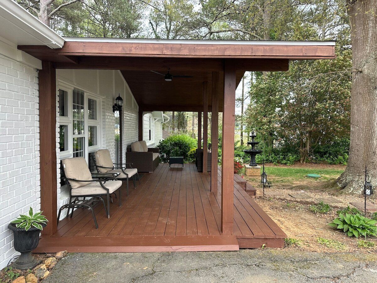 Un patio cubierto con suelo de madera, mobiliario exterior y un muro de ladrillo.