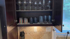 Una cocina con encimera de granito, un bloque de cuchillos y una vinoteca con diferentes copas.