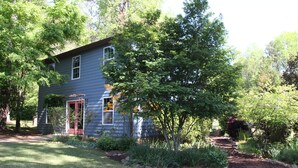 A two-story house with a red door, surrounded by a well-maintained garden and trees. - NEW Two Bedroom Suite Nestled in Stunning Backyard Garden (Athens)