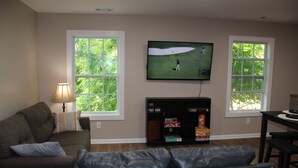 A living room with a television mounted on the wall, a fireplace, and two windows. - NEW Two Bedroom Suite Nestled in Stunning Backyard Garden (Athens)