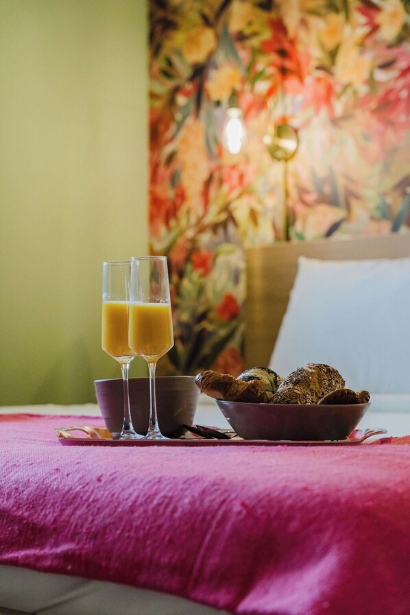A breakfast setting with two glasses of orange juice, a bowl of assorted pastries, and a cup on a pink tablecloth.