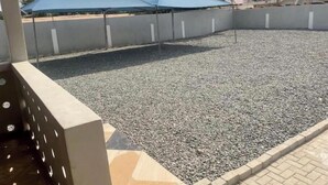 A covered outdoor area with gravel flooring, surrounded by walls and a building in the background. - Spintex - Home Away from Home-Suite Sylvia (Accra)