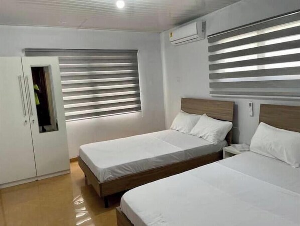 Une chambre avec deux lits, une armoire et une fenêtre avec des stores.