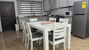 A modern kitchen with white cabinetry, a dining table with chairs, a microwave, and a refrigerator.