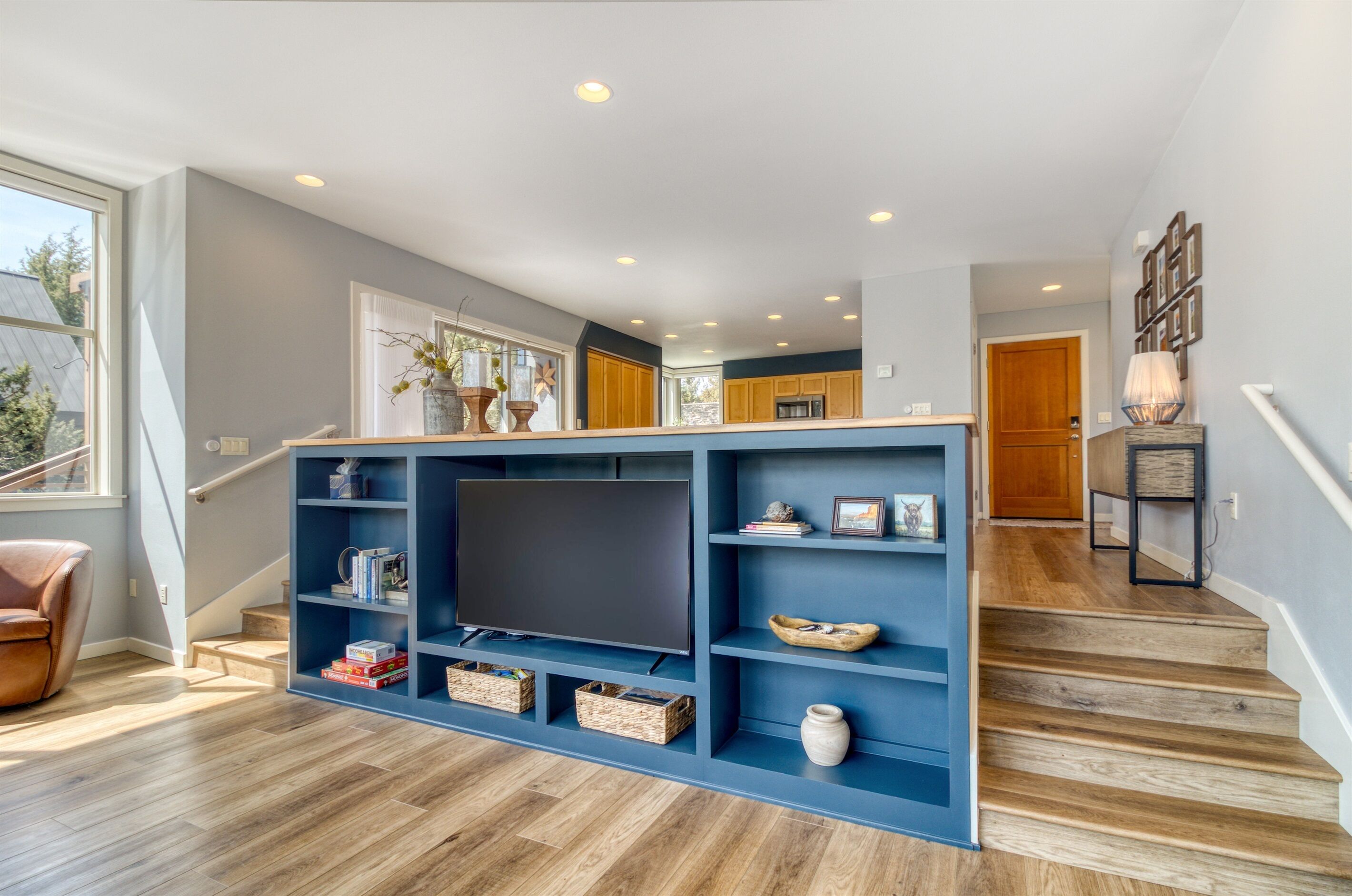 A modern living room with a large entertainment unit, wooden flooring, and a staircase leading to another room.