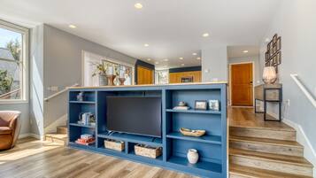 A modern living room with a large entertainment unit, wooden flooring, and a staircase leading to another room.