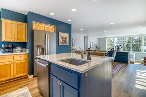 Una cocina moderna con armarios de madera, un refrigerador de acero inoxidable, encimera de mármol y un ventanal grande.