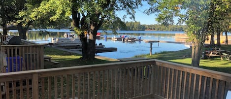 A wooden deck with a view of a lake, docked boats, and picnic tables.