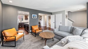 Een moderne woonkamer met een grijze bank, een oranje leren fauteuil en een houten salontafel.