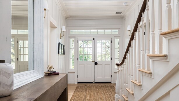 Un couloir avec un banc en bois, un tapis et un escalier doté de balustrades blanches.