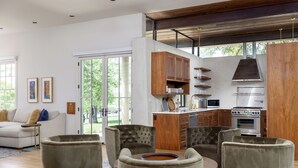 Un salon moderne comprenant un canapé, des fauteuils et une table basse. On y trouve également un coin cuisine avec des meubles en bois et des appareils électroménagers.
