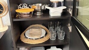 A kitchen cabinet with various storage containers, a colander, a juicer, and a woven placemat.