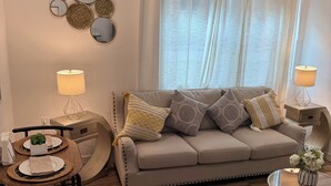 A living room with a beige sofa, round coffee table, and a dining area with a wooden table and chairs.