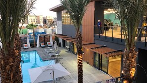 A rooftop pool area with lounge chairs, palm trees, and a modern building in the background.