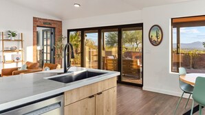 A modern kitchen with a large island, a dining area with a table and chairs, and a sliding glass door leading to an outdoor patio with a view of the desert. - Private and Quiet with stunning views (Tucson)