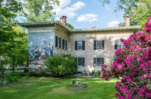 Um edifício histórico com um mural, um gramado bem cuidado e flores rosa vibrantes.