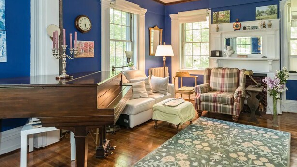 A living room with a piano, a sofa, a plaid armchair, and a fireplace. - Higganum House B&B (Higganum)