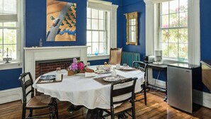 A dining room with a white table set for four, a fireplace, and a kitchen area with a refrigerator. - Higganum House B&B (Higganum)