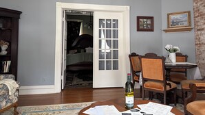 A room with a wooden floor, a dining table with chairs, a bookshelf, and a door leading to another room. - The Gallery (Hermann)