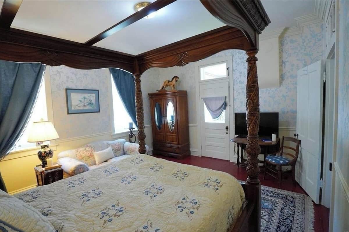 Un dormitorio con una cama con dosel, un armario de madera, un televisor y una silla.