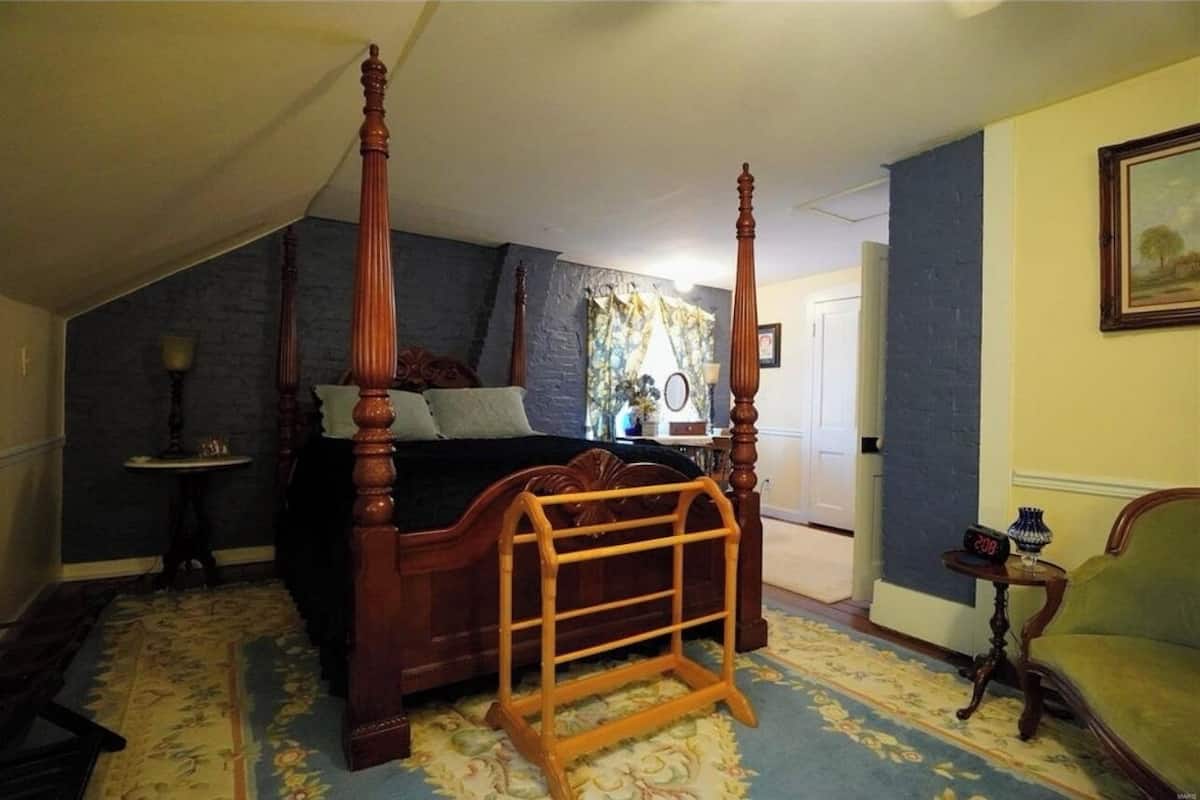 Un dormitorio con cama con dosel, una escalera de madera, una mesita con un reloj y una silla.