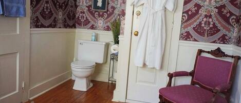 Een badkamer met een toilet, een witte deur, een houten stoel en behang met een patroon.