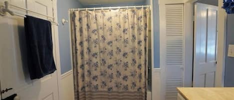 A bathroom with a shower curtain, a towel rack, a sink, and a door.