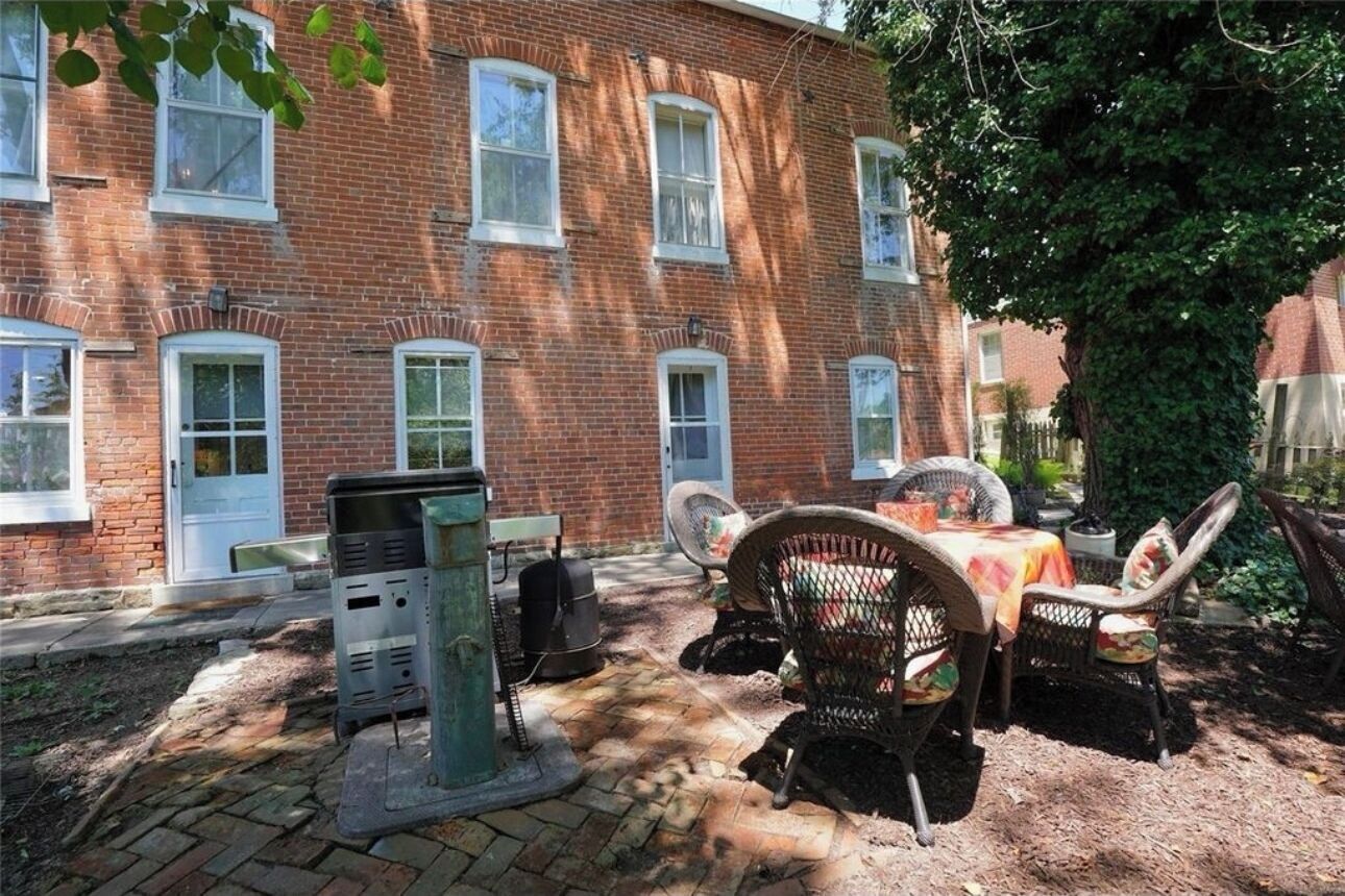 Un bâtiment en briques doté d’une terrasse pavée, de sièges extérieurs et d’une poubelle.