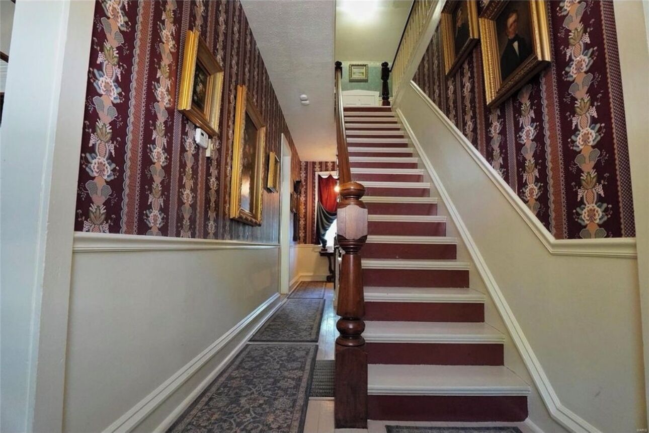 A grand staircase with ornate wallpaper and a wooden handrail.