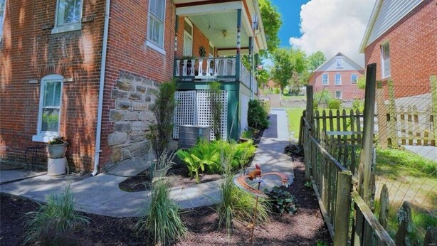 A brick house with a covered porch, a fenced yard, and a small garden area. - The Gallery (Hermann)
