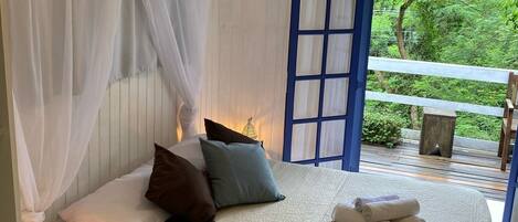 Un dormitorio con una cama, cortinas blancas y vistas al verdor exterior.