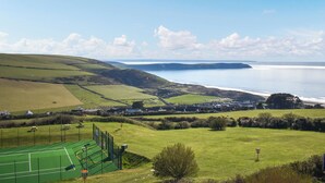 A coastal landscape with a tennis court, houses, and a view of the sea. - 2 bedroom accommodation in Woolacombe (Woolacombe)