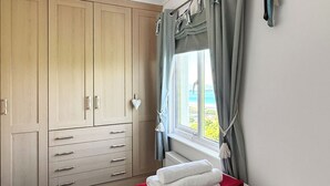 A hotel room with a bed, a large wardrobe, and a window with curtains. - 2 bedroom accommodation in Woolacombe (Woolacombe)