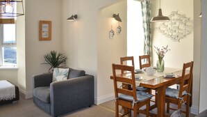 A dining area with a wooden table and chairs, a grey sofa, and a potted plant. - 2 bedroom accommodation in Woolacombe (Woolacombe)