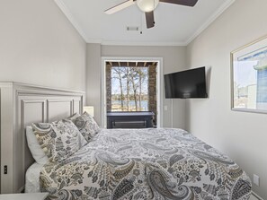 Un dormitorio con cama, ventilador de techo, televisor y vista al exterior.