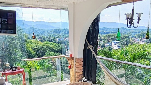 A spacious living area with a large window offering a view of lush greenery and distant mountains. There is a sofa, a small table, and a hammock. - Encantadora casa de 4 alcobas con WIFI (Tocaima)