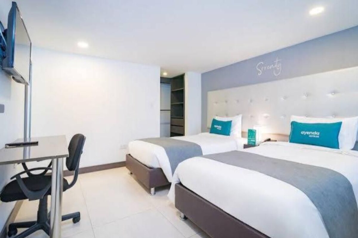 A hotel room with two beds, a desk, and a chair.