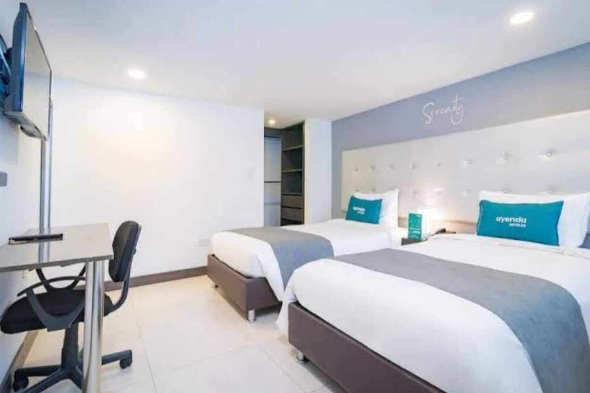 Habitació d'hotel amb dos llits, una taula de treball i una cadira.