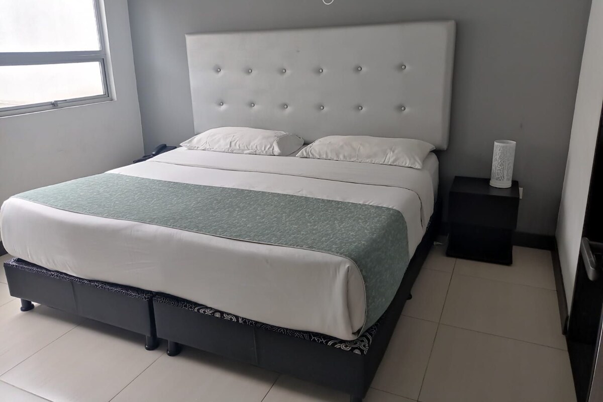 A modern bedroom with a large bed, grey walls, and a window.