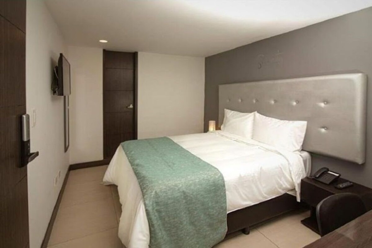 A modern hotel room with a large bed, a bedside table with a phone, and a TV mounted on the wall.