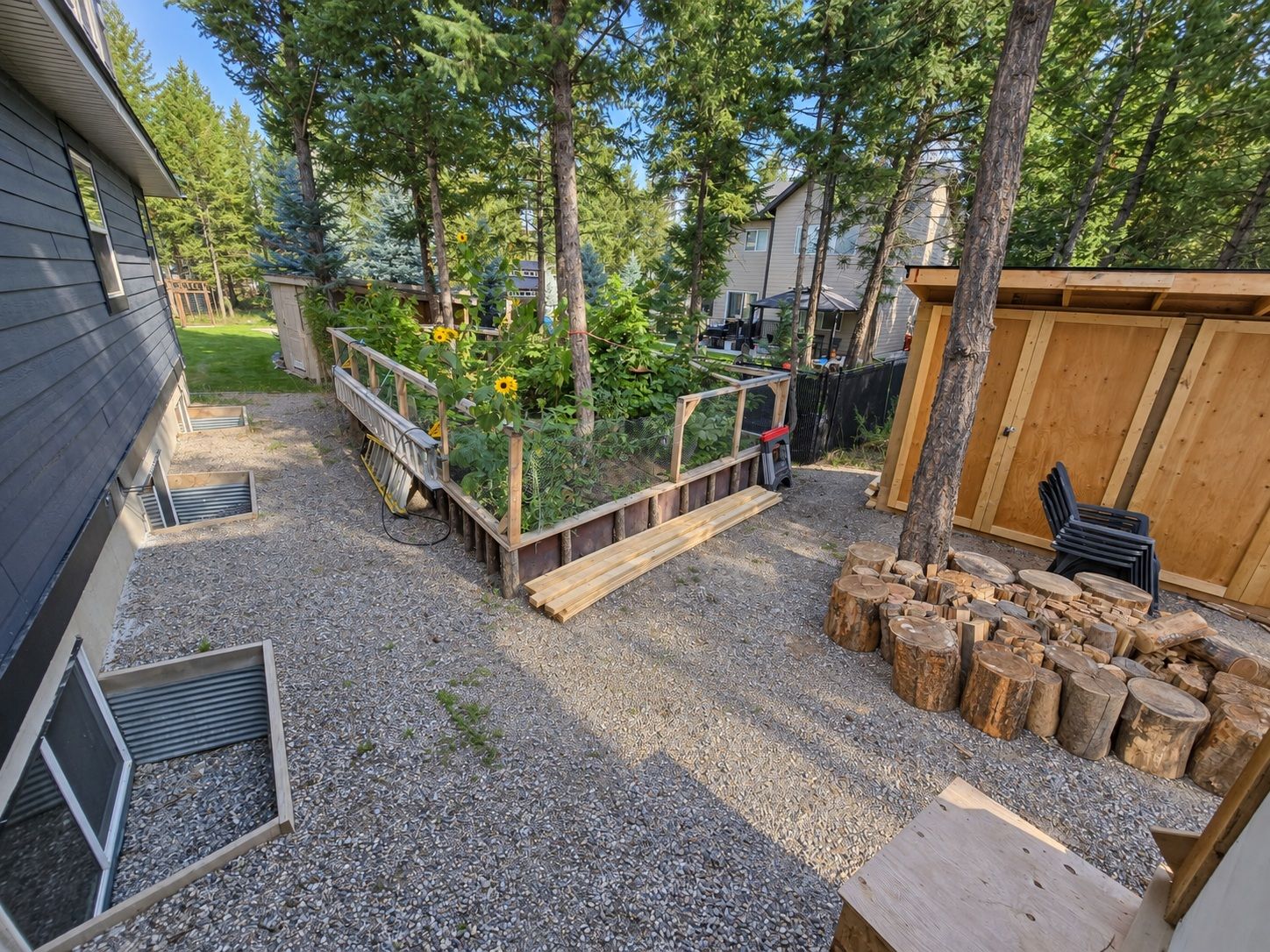 Ein Garten mit erhöhten Blumenbeeten, einer Holzterrasse und einem Holzstoß.
