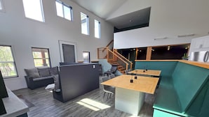A modern interior with a wooden floor, a black sofa, a wooden dining table, and a green accent wall. - Copper Rose Retreat B&B (Invermere)